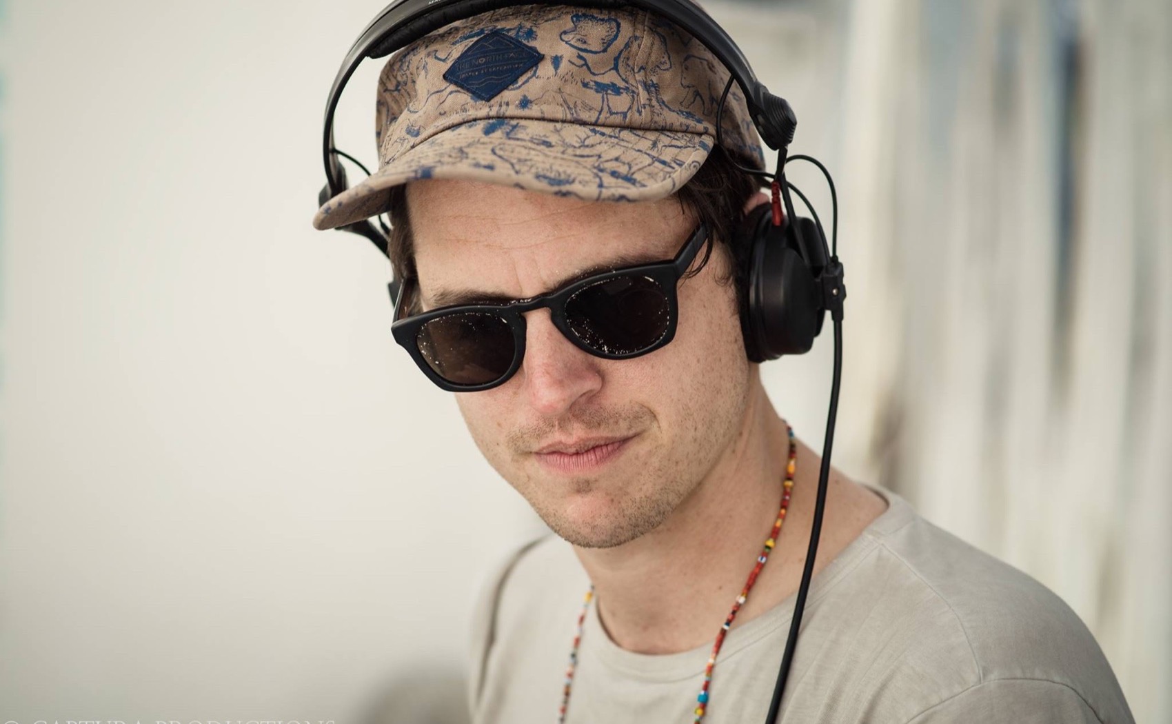 Andrew Smith as Misawa in headphones, a patterned cap, and sunglasses behind the decks at Coco Tulum.