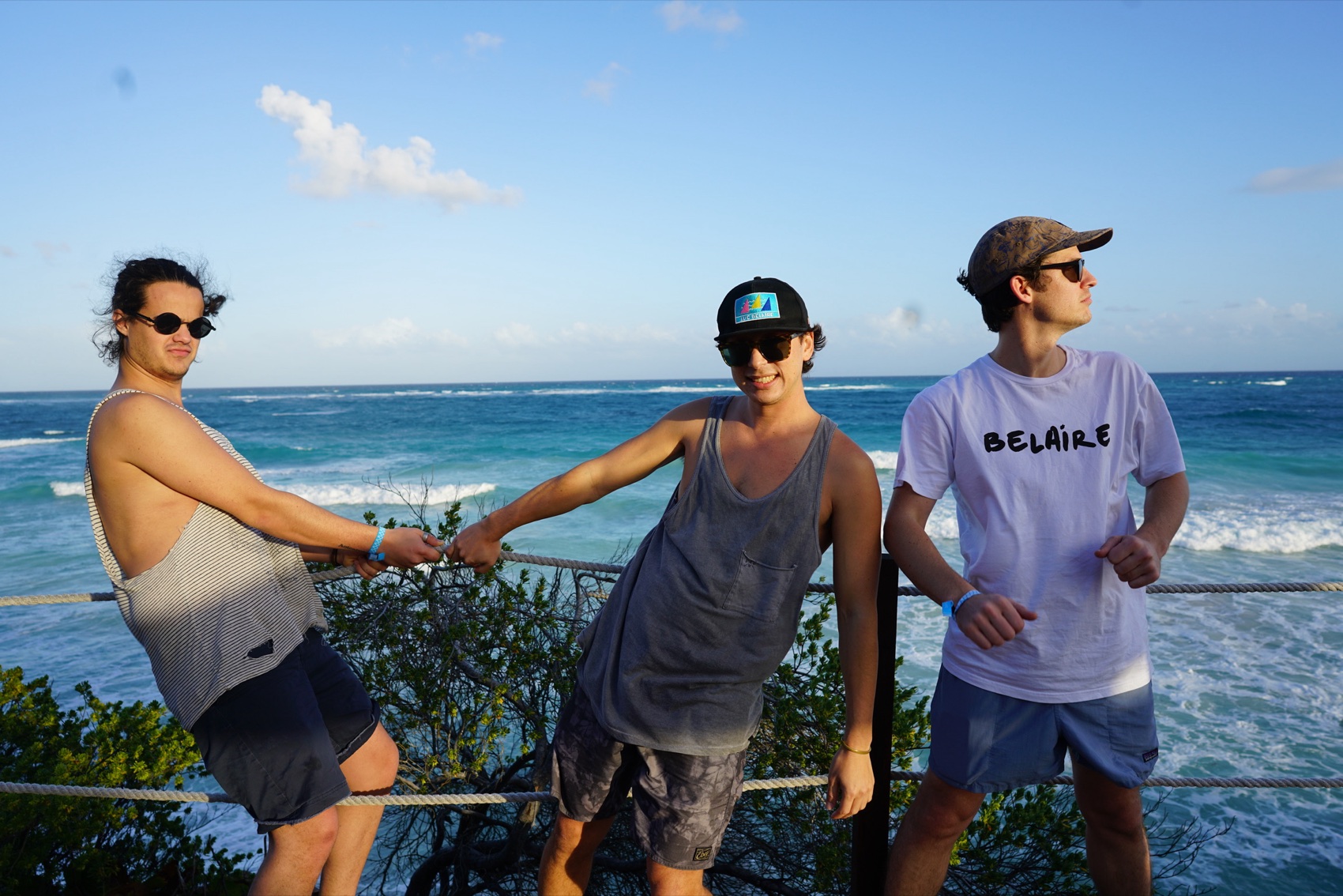 Andrew Smith, at right in a cap and sunglasses, with two friends at a rope railing above the surf in Tulum.